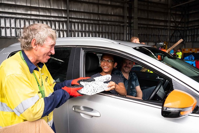 A worker is handed material from a couple in a car.