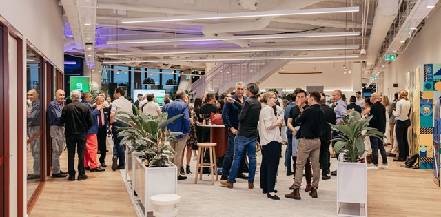 People mingling in a modern, well-lit office space with plants and colorful decor.