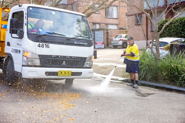 Worker using a pressure washer to clean the street near a parked truck.