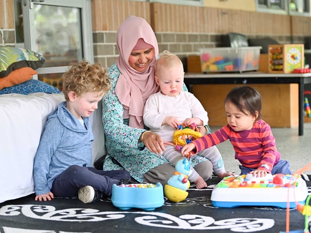 3 toddlers and teacher sitting on a mat playing with toys