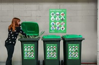 A woman disposing of garden clipping in a green lid City of Sydney bin.