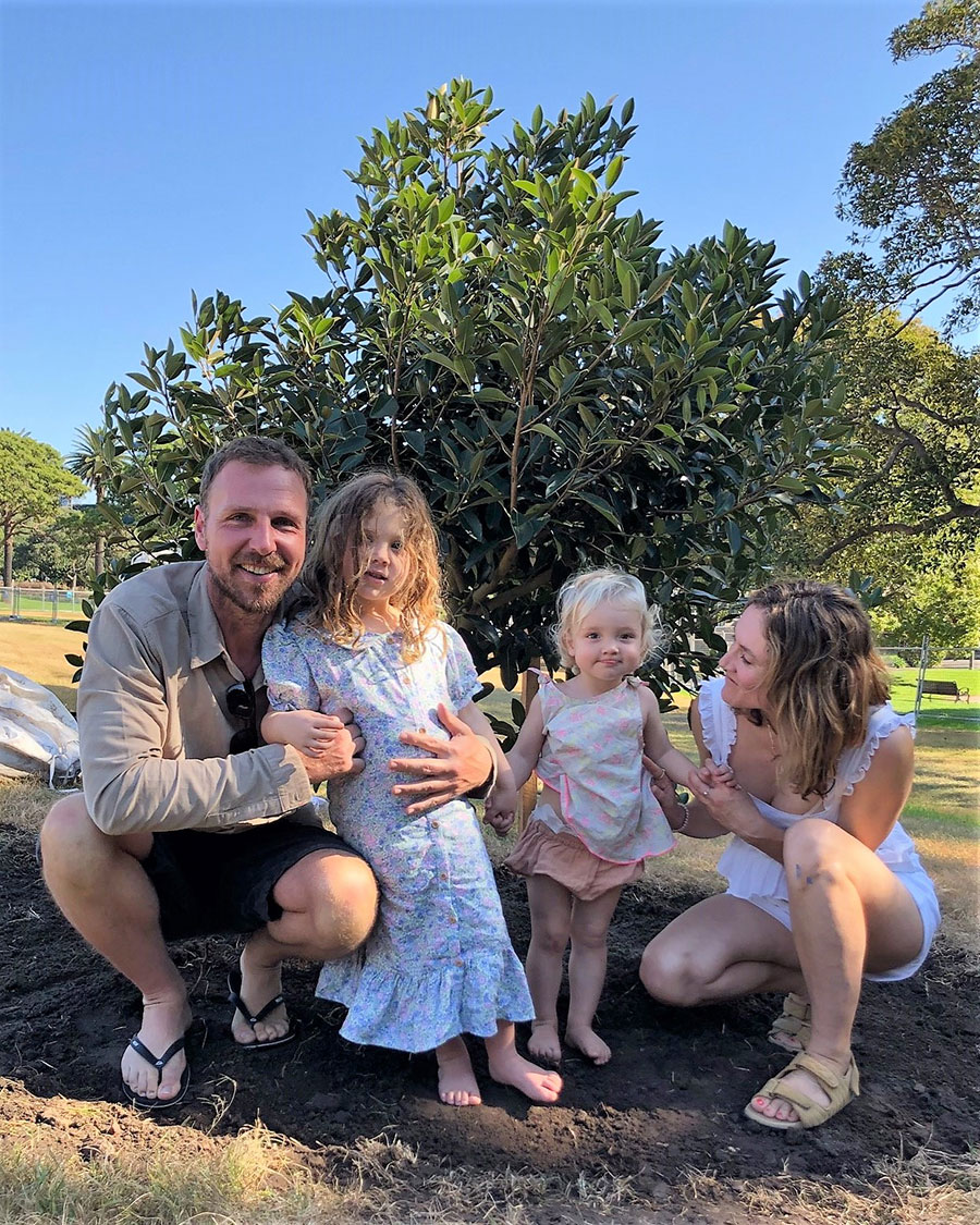 Two adults and two small children positioned in front of a small tree.